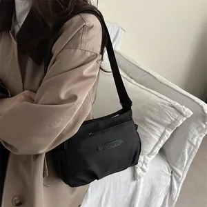 Minimalist black nylon crossbody bag with wide strap worn with a khaki trench coat