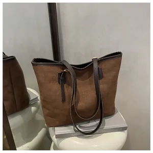 Detailed close-up of brown suede tote bag with adjustable dark leather straps on a white stool