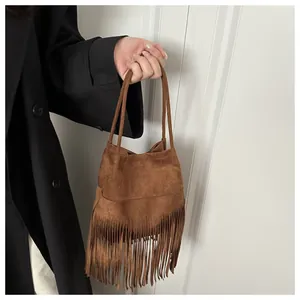Détail d'un sac seau en daim marron avec de longues franges tenu par un mannequin en manteau