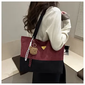 Detalle del bolso tote bicolor con textura de ante, logo dorado y colgante de osito