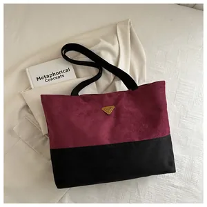 Detalle de bolso tote grande en color burdeos y negro con logo dorado sobre una chaqueta