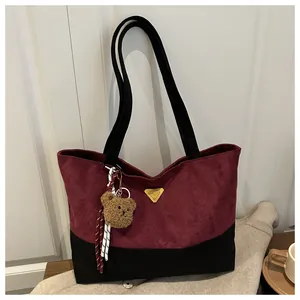 Detalle del bolso tote de ante con bloques de color, logo dorado y colgante de oso