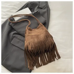 Gros plan d'un sac hobo en daim marron à franges posé sur un blazer gris