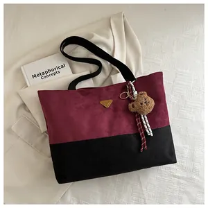 Detalle de bolso tote de ante burdeos y negro con logo dorado y colgante de oso