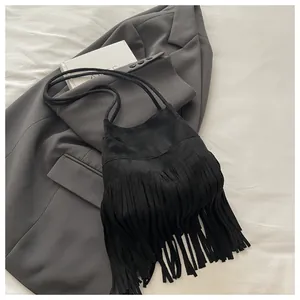 Gros plan du sac à bandoulière noir à franges sur un blazer gris et livre d'art