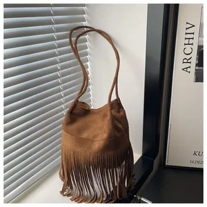 Détail d'un sac seau bohème en daim marron avec de longues franges près d'une fenêtre