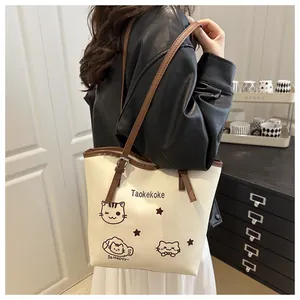 Close-up of cream tote bag with cartoon cats and brown straps worn on the shoulder