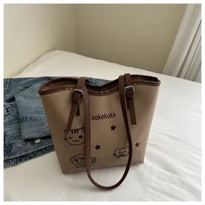 Close-up of beige tote bag featuring playful cat illustrations and brown leather straps