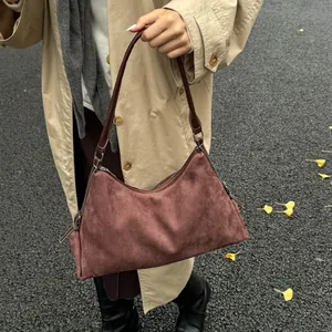 Detailed close-up of dark brown suede handbag with zipper and leather shoulder strap