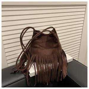 Détail du sac seau en daim marron avec de longues franges bohèmes et une bandoulière tressée