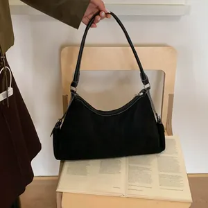 Detail of black suede shoulder bag with white contrast stitching and sleek zipper top