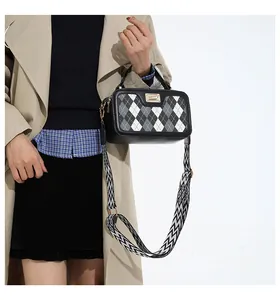 Detail of checkered crossbody bag featuring a wide woven shoulder strap and top handle