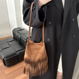 Sac seau bohème en daim marron avec franges et bandoulière fine porté sur un manteau chic