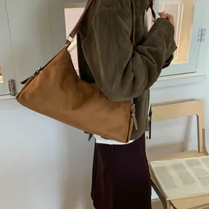 Detail of a brown suede baguette bag worn on the shoulder in a minimalist indoor setting