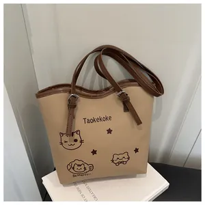 Detail of beige tote bag featuring cute cartoon cat print and brown leather handle
