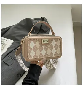 Detail of checkered square bag featuring golden buckle and wide woven shoulder strap