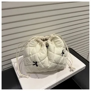 Detail of white quilted drawstring pouch with black bow embroidery and stitched pattern