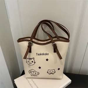 Fashionable cream bucket bag with cat prints and brown adjustable strap on white book