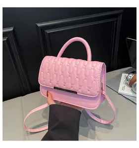 Pink quilted leather handbag with gold metal bar and top handle on a grey sofa