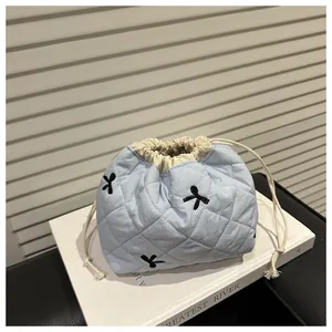 Close-up of light blue quilted drawstring bag featuring black bow embroidery detail
