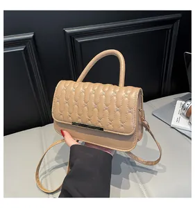 Close-up of quilted handbag with wave stitching and gold metal bar detail in beige