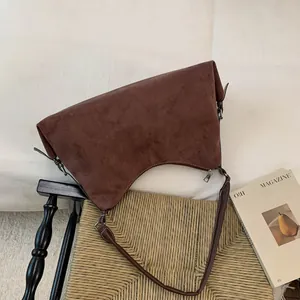 Detail of a brown suede crescent bag with silver zipper on a woven chair with a magazine