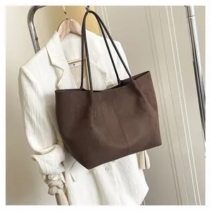 Détail d'un sac cabas en daim marron avec fines anses en cuir sur fond de blazer beige
