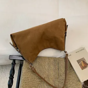 Close-up of brown suede shoulder bag featuring a unique curved base and contrast stitching
