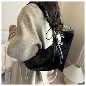 Détail d'un sac à bandoulière noir brillant avec anse plissée sur un mannequin