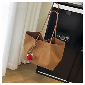 Détail d'un sac cabas marron en daim avec des breloques pelucheuses sur une chaise