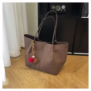 Détail d'un sac cabas en daim marron foncé avec fines bretelles et un charme en peluche