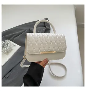 Detailed view of white quilted faux leather handbag with golden trim and curved handle
