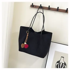 Détail d'un sac cabas en daim noir avec pompon bicolore suspendu à un crochet mural