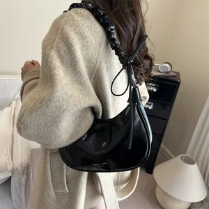 Sac hobo noir plissé avec nœuds décoratifs porté par un mannequin dans un cadre élégant