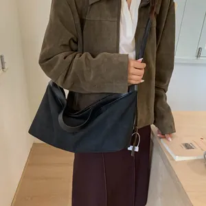 Model wearing a large black suede tote bag with a long strap in a minimalist cafe setting