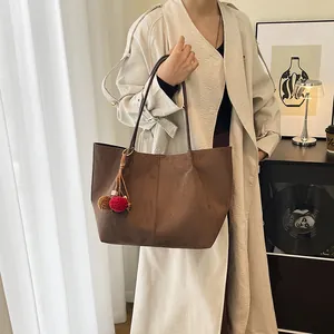 Sac cabas en daim marron avec pendentif en peluche porté par une femme en intérieur