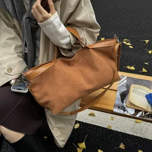 Brown suede tote bag shown in an autumn setting with dual handles and long shoulder strap