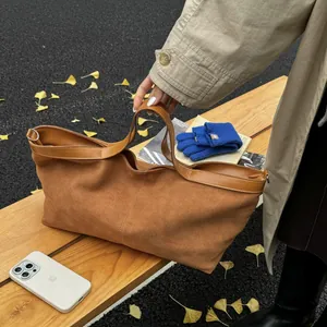 Detail of tan suede tote bag texture with smooth leather trim against autumn leaves