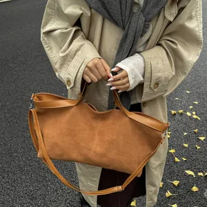 Brown suede tote bag with leather trim and adjustable strap in autumn street setting