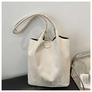 Detail of minimalist cream suede bucket bag with fine stitching and dual handle straps