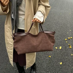Detail of dark brown suede tote bag with leather piping and slim handles outdoors