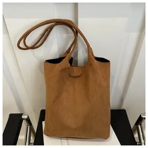 Close-up of matte brown suede bucket bag with sleek cylindrical handle on a minimalist chair