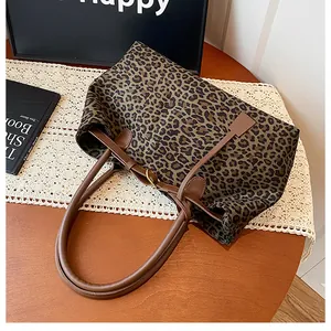 Detailed close-up of leopard print tote bag with brown leather handles on a wooden table