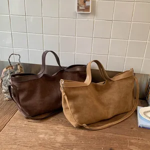 Close-up of suede tote bags in brown and tan with smooth leather handles on wooden table