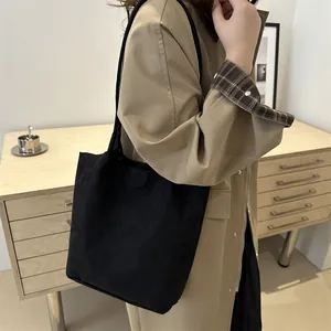 Minimalist black suede tote bag with slim shoulder straps shown on a model in beige coat
