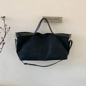 Detail view of large black tote bag hanging on wall hook showing texture and strap details