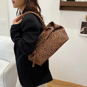Leopard print tote bag with brown leather handles worn by a model in a minimal interior