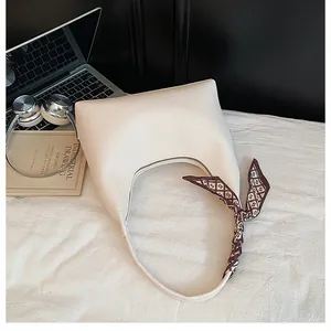 Vue de dessus d'un sac hobo crème avec texture litchi et foulard en soie sur tissu blanc