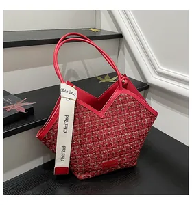 Detail of red tweed bucket bag with leather handles and decorative brand webbing