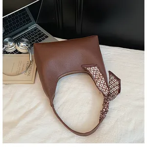 Détail d'un sac à main en cuir marron foncé orné d'un foulard en soie sur un bureau